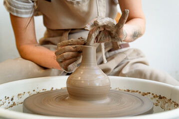 close up of ceramist hands working and shaping ceramic vase on the lathe or potter's wheel inside a...
