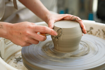 close up of raw ceramic running on the lathe or potter's wheel, with hands with tool refining fine details of vase