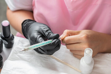 close-up of the hands of a woman decorating her nails with a manicure brush