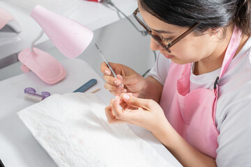 young woman manicurist cleaning her own nails with a cuticle pusher - obrazy, fototapety, plakaty