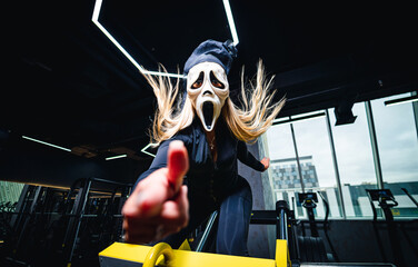 Fototapeta na wymiar Halloween person in dark gym. Lady in carnaval mask trainer.