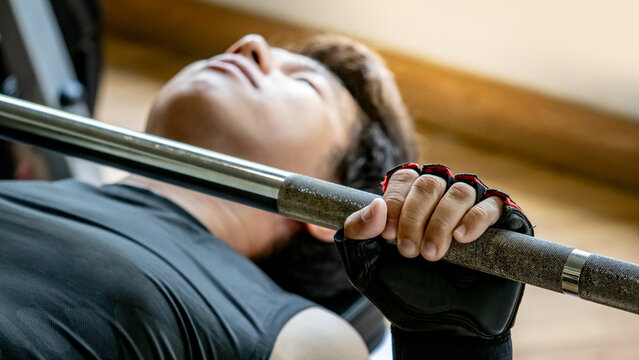 Active Asian sport man in black sportswear lying on exercise bench doing barbell bench press lifting at weightlifting station. Indoor weight training and muscular building workout in fitness gym