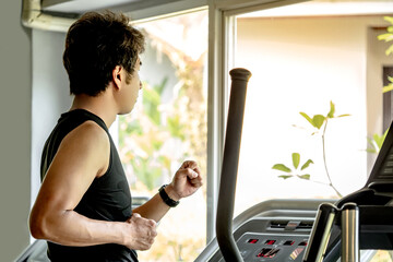 Asian runner man with well trained body in black sportswear running on treadmill in fitness gym....