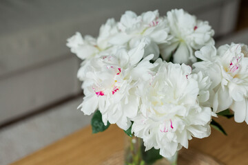 Home cozy interior. Bouquet of peonies in a glass vase on a wooden coffee table. Spring.