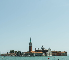 View of island across the clear water on sunny sky with clock tower of church as highest point 