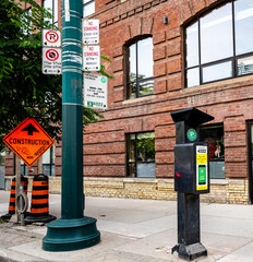 Solar powered paid parking station on the side of the street in Toronto, Ontario, Canada next to no parking signs and a construction sign in front of a brick building