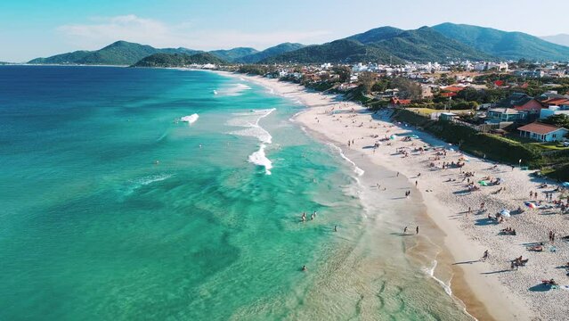 Aerial view of the sea with gentle waves and sandy beach with people relaxing on it. Lomba do Sabao beach on Santa Catarina island in Brazil