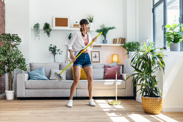 Funny motivated woman dancing and listening to music with headphones while sweeping the house