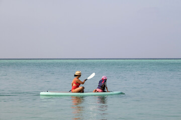 Mother with daughter puddleboarding together on Maldives. Family active vacation concept 