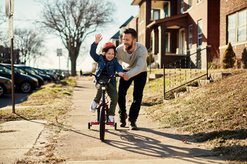 Father teaching his son how to ride a bike in the suburbs - obrazy, fototapety, plakaty