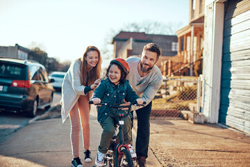 Young boy riding a bike with his parents next to him on a sidewalk in the suburbs