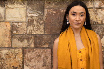 Native American young woman dressed in yellow hues on brown stone background. Copy space