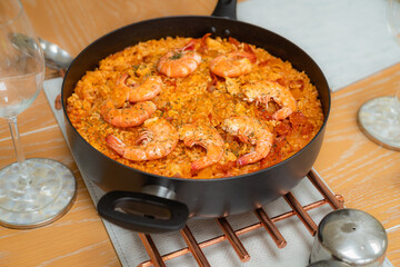 Cooked shrimps in a seafood rice paella in a pan on a trivet on a wooden table.