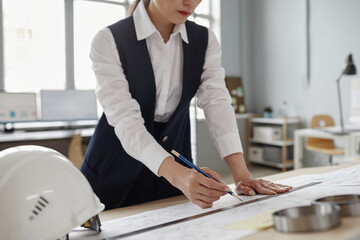 Closeup of female engineer drawing blueprints and plans at workstation in office, copy space