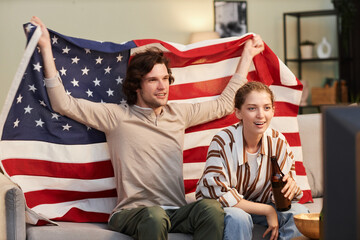 Portrait of young couple with USA flag cheering while watching sports match at home