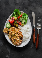 Delicious lunch - lime, cilantro, garlic olive oil marinated grilled chicken breast, basmati rice and fresh vegetable salad on a dark background, top view