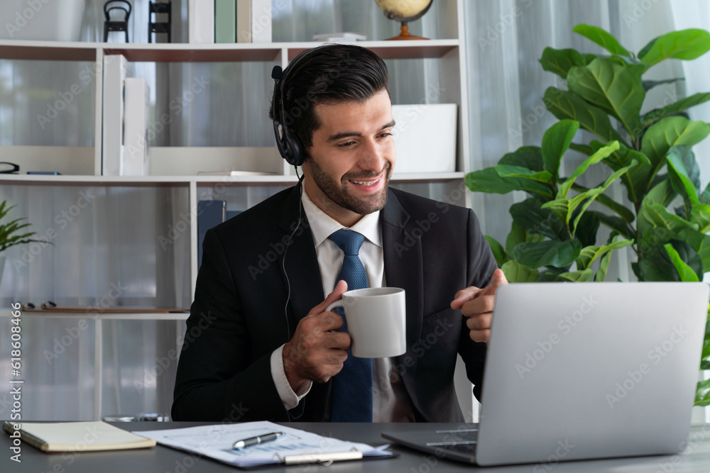 Poster manager of call center operator office sitting on his desk with his coffee while working on laptop. 