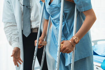 Doctor takes care of patient in crutch at hospital. Physical therapist and leg injury recovery...