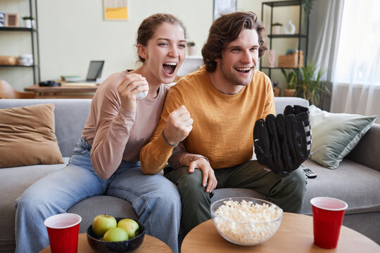 Portrait Of Emotional Young Couple Watching Sports Match Together At Home And Cheering