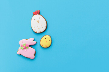 Easter gingerbread with icing, bunny, chicken, egg, seasonal flowers on blue backdround. Happy festive floral concept, glazed cookie figures composition. Flat lay, top view, place for text, banner