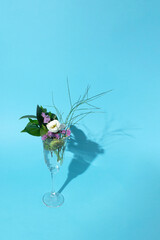 Transparent glass of  leaves and flowers placed on  blue background. Bouquet, glass and copy space.