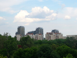 Fototapeta na wymiar Group of blocks of apartments on sky with white clouds, seen over green trees in Bucharest