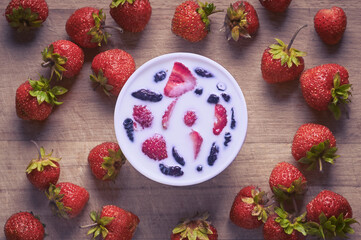 Strawberries on a cutting board close up with a round cup of yogurt or milk. Photo of dishes with...