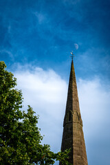 Moon over spire of church with blue sky
