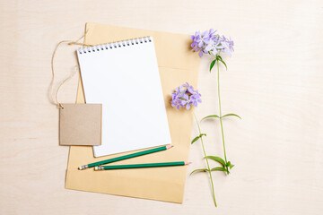 Mockup blank notebook, envelope, pencils and blue flowers.