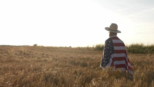 Stylish white woman in cowgirl hat with USA flag running in yellow wheat field