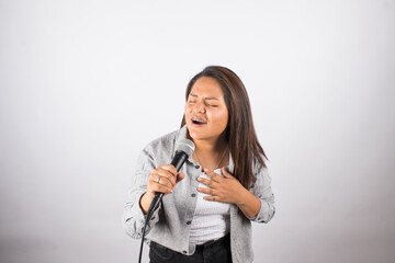 photo of latin woman singing passionately with a microphone on light studio background. Concept of...