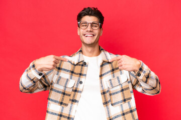 Fototapeta premium Young caucasian handsome man isolated on red background proud and self-satisfied