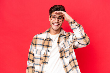 Young caucasian handsome man isolated on red background looking far away with hand to look something