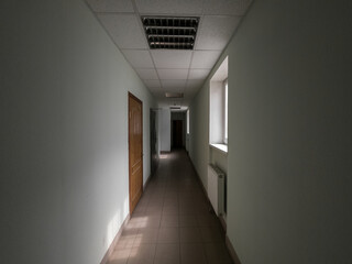Empty dark office corridor lighted by windows.