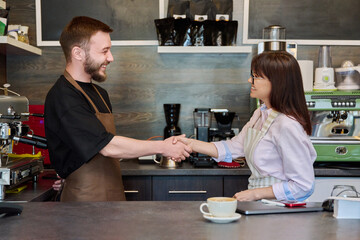 Colleagues, partners, man and woman shake hands, in coffee shop