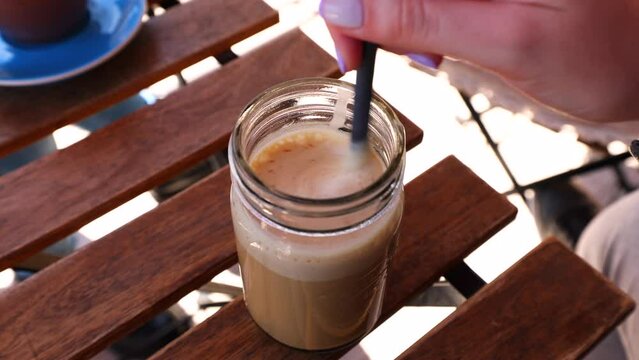 A person girl with painted fingernails stirring a glass of ice coffee with bio milk and a paper straw. High quality 4k footage