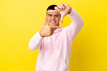 Fototapeta premium Young handsome man over isolated yellow background focusing face. Framing symbol