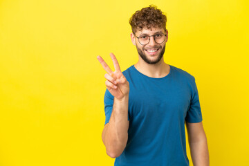 Young handsome caucasian man isolated on yellow background smiling and showing victory sign