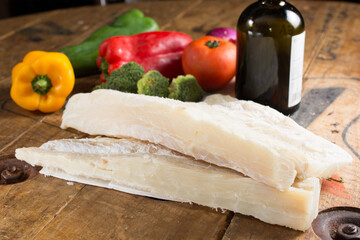 cod fillet on wood, with vegetables and olive oil in the background