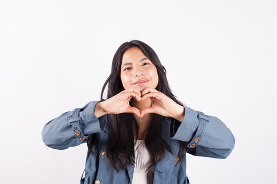 Photograph of young woman making a heart with her fingers on a light studio background. Concept of people and emotions