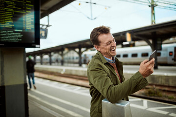 Mature man using a smart phone while waiting for his train at the train station