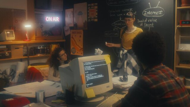 Creative young woman standing at chalkboard in retro garage office sharing her ideas about business plan to her male colleagues, 90s aesthetics