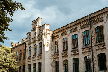 Obraz premium Facade of an old brick building with a tower. Building against the sky. Beautiful old architecture. University park. Tourist place of Kyiv. Gothic architecture.