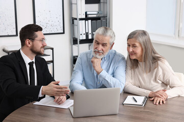 Insurance agent consulting elderly couple about pension plan at wooden table in office