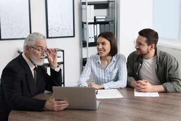 Young couple consulting insurance agent about pension plan at wooden table indoors