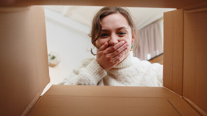 Inside view from box. Young happy woman unpacking delivery parcel at home. Smiling satisfied girl...