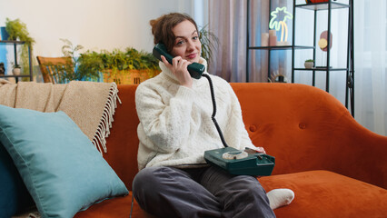 Portrait of young woman making wired telephone conversation with friends sitting call on couch at...