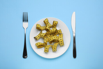 Measuring tape, fork and knife on light blue background, flat lay. Weight loss concept