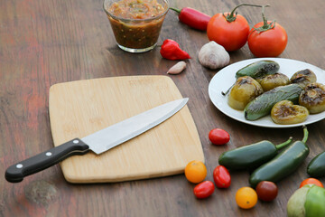 Salsa sauce, board with knife and ingredients on wooden table