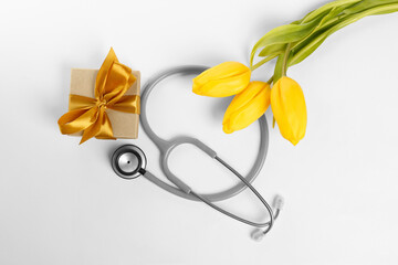 Stethoscope, gift box and yellow tulips on white background, flat lay. Happy Doctor's Day